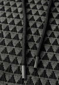 Zwart en grijs gestreepte stof met een driehoekig patroon, voorzien van zwarte koordjes en metalen tips voor het vastmaken.