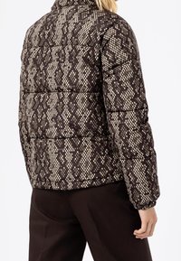 Puffermantel med ett reptilmönster i brunt och beige, med quiltade sektioner, hög krage och elastiska ärmslut.