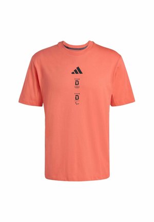 Korálově červené tričko s krátkými rukávy z bavlny. Má černé logo Adidas a grafiku s textem, kulatý výstřih a volný střih.