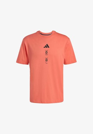 Korallinvärinen, lyhythihainen t-paita, joka on valmistettu puuvillasta. Siinä on musta Adidas-logo ja tekstigrafiikka, pyöreä kaulus sekä rento istuvuus.