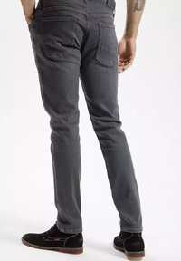 Szare dżinsy o slim fit, z pięcioma kieszeniami i widocznymi detalami szwów. Noszone z czarnym obuwiem z czerwonymi akcentami.