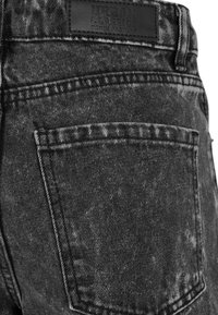 Zatvoreni prikaz stražnjeg đepa crnih traperica s kiselim pranjem, s izvezenom etiketom koja glasi Urban Classics Denim Factory.