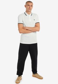 Witte polo met zwarte ribbelkraag en accenten op de mouwen, gecombineerd met zwarte joggingbroek en beige sneakers. Gladde stof, klassieke pasvorm.