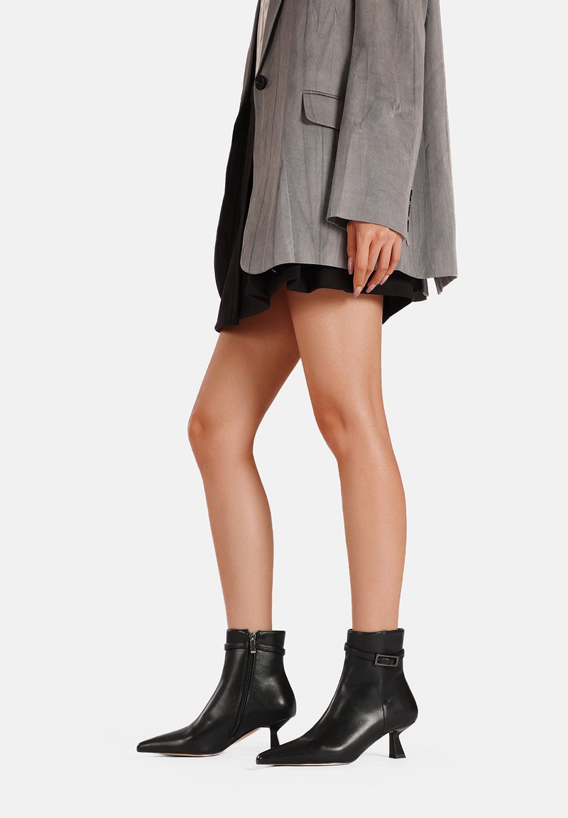 Stivali alla caviglia in pelle nera con punta affusolata, dotati di chiusura con zip e tacco a blocco basso. Texture liscia e design minimalista.