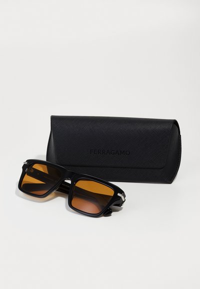 Lunettes de soleil carrées noires avec des verres teintés bruns, ornées d'accents en argent. Accompagnées d'un étui noir texturé avec le logo "FERRAGAMO".