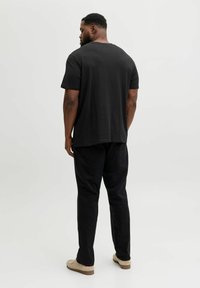 Sort bomulds T-shirt med korte ærmer og rund hals; kombineret med sorte bukser og beige slip-on sko; vist bagfra.