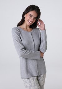 Maglietta grigia chiaro a maniche lunghe con bottoni, realizzata in tessuto morbido, con scollatura tonda e chiusura a bottoni delicati, abbinata a pantaloni con motivi.