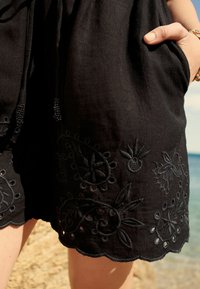 Sorte broderede shorts lavet af letvægtsstof, med indviklede blomster mønstre og bølgede kanter, samt sidelommer.
