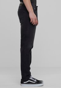 Jeans de denim negro con un ajuste recto, que presentan un diseño clásico de cinco bolsillos y una sutil textura deslavada, combinados con zapatillas negras.