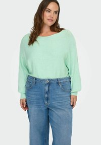 Vaaleanmintunvihreä, ribbineulottu neulepaita, jossa on leveä venepääntie ja laskostetut olkasaumat, yhdistetty korkeavyötäröisiin sinisiin farkkuihin.