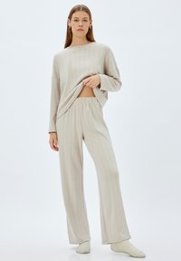 Keveä beige kotivaatteet-setti, joka sisältää rento neuleen, jossa on ribbitekstuuri, ja leveälahkeiset housut, joissa on joustava vyötärö.