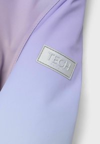 Paarse technische stof met een glanzend zilveren label met de tekst "TECH" en "nameit." Glad oppervlak, met een subtiele kleurovergang van licht naar donker paars.