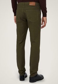 Pantalones de algodón verde oliva con un ajuste slim, que cuentan con dos bolsillos traseros y un parche de cuero marrón en la parte trasera de la cinturilla.