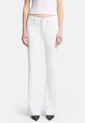 White flared jeans made from denim, featuring a fitted waist, standard pockets, and a smooth texture. Paired with pointed black heels.