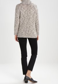 Pull épais gris clair avec un col montant, un tricot texturé et une couture au dos. Associé à un jean noir slim et des chaussures en cuir noires.