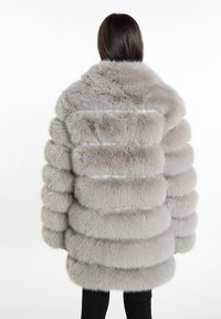 Šedý kabát z umělé kožešiny s načechraným, strukturovaným povrchem a vertikálními pruhy. Design obsahuje vysoký límec a nadměrné rukávy.