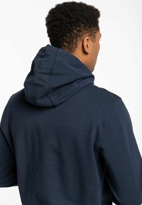 Sudadera azul marino hecha de una suave mezcla de algodón, con capucha ajustable y puños acanalados. La vista trasera muestra una superficie de tela lisa y sin adornos.