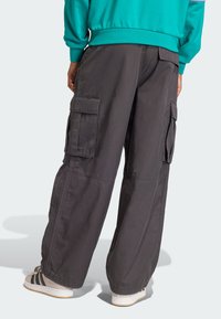 Sivé pracovné nohavice s voľným strihom, vybavené viacerými bočnými vreckami a prešitými švami. Nosené s bielymi a čiernymi pruhovanými teniskami.