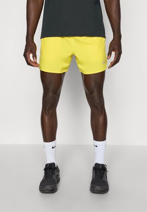 Bright yellow athletic shorts with a smooth texture, featuring a Nike logo. Worn with black sneakers and white socks with a black accent.