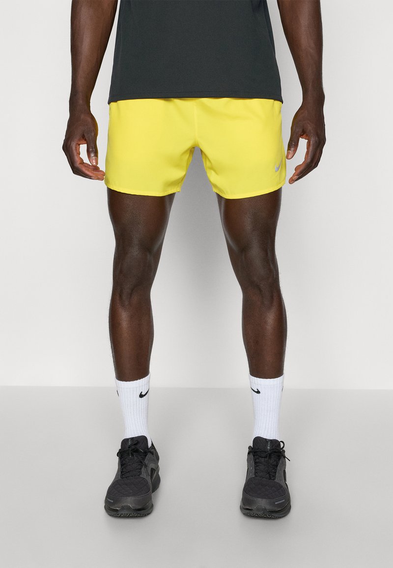 Bright yellow athletic shorts with a smooth texture, featuring a Nike logo. Worn with black sneakers and white socks with a black accent.