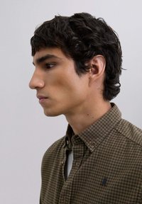 Camisa de cuadros marrón y verde con cuello, que presenta un pequeño logo en el pecho y una tela texturizada.