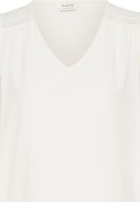 Blouse blanche à col en V avec une bordure en dentelle discrète aux épaules et des détails de tissu froncés, étiquetée "b.young The Collection."