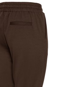 Pruunid elastsed p�üksid, millel on üks õmmeldud tasku taga ja külgtasku paremal küljel.