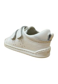 Zapato de cuero blanco con dos correas de Velcro grises, diseño perforado en los laterales, punta redondeada y detalles de costura a lo largo de la suela.