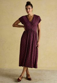 Luftiges, midilanges Kleid in tiefrot mit floralem Muster. V-Ausschnitt, kurze Ärmel und geraffte Taillenpartie. Kombinieren Sie es mit burgunderfarbenen Schuhen.