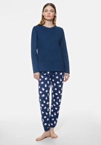 Haut à manches longues bleu marine associé à un pantalon de pyjama avec un motif de pois blancs et roses, fabriqué en coton doux. Coupe décontractée dans l'ensemble.