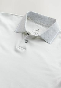 Weißes Poloshirt mit einem gemusterten Kragen in Hellgrau. Verfügt über zwei Knöpfe und einen kleinen Schlitz am Saum. Markenlabel innen am Kragen sichtbar.