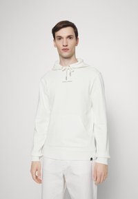 White hooded sweatshirt in soft material, featuring a front pocket, drawstring with silver tips, and a subtle logo in the center.