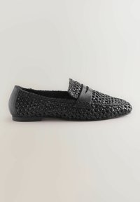 Mocasines negros trenzados con una superficie texturizada, que presentan una banda de cuero suave en la parte superior y una suela baja y plana.