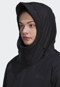 Black jacket with a high collar and oversized hood. Features a zipper closure and subtle tonal logo on the chest. Smooth, matte texture.