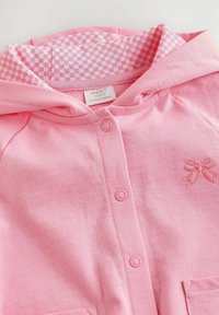 Różowa dziecięca bluza z kapturem, wykonana z miękkiego materiału, z podszewką w kratkę, z przodu na guziki oraz z małym haftowanym detalem w postaci kokardki.