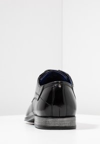 Chaussure en cuir verni noir montrant un talon bas, une texture lisse, une forme arrondie avec des détails subtils de couture et une doublure intérieure bleue.