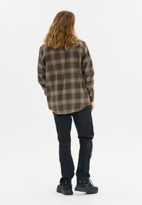 Bruine geruite flanellen shirt met een relaxed fit, lange mouwen en een gebogen zoom, gecombineerd met zwarte cargobroeken en donkere schoenen.