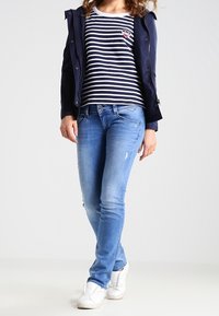 Granatowa kurtka, biało-granatowa koszulka w paski z naszywką w kształcie serca, jasnoniebieskie jeansy z przetarciami, białe tenisówki.