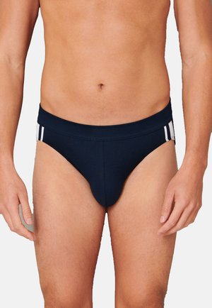 Slip da bagno blu navy realizzati in tessuto elasticizzato, con una cintura larga e due strisce bianche su ciascun lato.