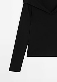 Haut noir à manches longues avec un large col plié, présenté de la taille jusqu'en haut sur fond blanc.
