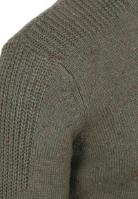 Gebreide trui in donkergroen met veelkleurige spikkels. Heeft een geribbelde textuur en een ronde halslijn, wat een gezellige uitstraling benadrukt.