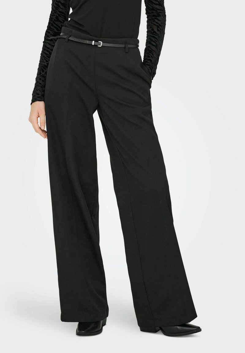 Pantalons larges noirs avec une texture lisse, dotés de poches avant et d'une ceinture noire fine avec un détail de boucle en argent.