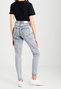 Jeans de denim gris claro de cintura alta con una textura desvanecida, que cuentan con bolsillos traseros y pasadores para cinturón, combinados con una camiseta negra y zapatillas blancas.