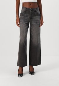 Platas kājas melni denima džinsi ar piecām kabatām, maigi nodilumi un augsts jostasvieds. Audumam ir jauka struktūra un neliela izbalēšana.