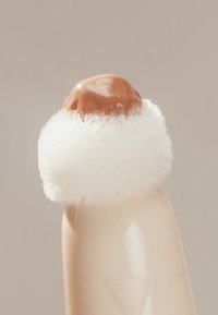 Schwammapplikator mit glänzend brauner Spitze, umgeben von weichem weißem Flaum, angebracht an einem transparenten beigen Kunststoffgehäuse. Texturierte Oberflächendetails sichtbar.