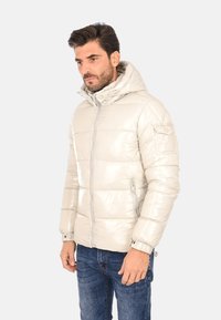 Giacca imbottita grigia chiaro con finitura lucida, cappuccio regolabile, tasche laterali con zip e polsini elasticizzati. Stile aderente con dettagli cuciti.