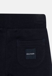 Mörkblå joggingbyxor med en texturerad midja och en bakficka. Har en sydd fyrkantig etikett med "HILFIGER" i vit text.