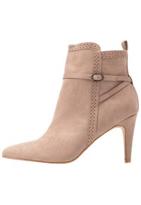 Bottine en daim beige avec un bout pointu, un design découpé, des détails perforés sur le haut et un talon haut élancé.