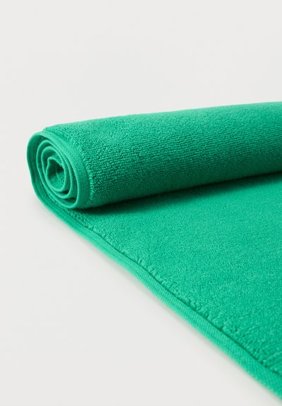 Μια ζωηρή πράσινη μικροϊνική πετσέτα, τυλιγμένη ρολάκι με υφή επιφάνειας, ακάλυπτη μερικώς σε λευκό φόντο.