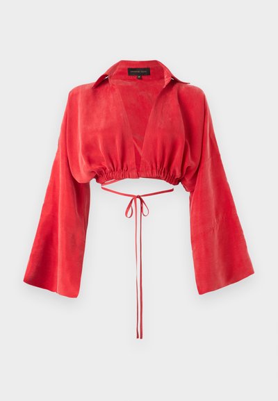 Blouse rouge courte en tissu lisse, avec un décolleté en V, de longues manches larges, et une taille cintrée avec un détail de lien à l'arrière.